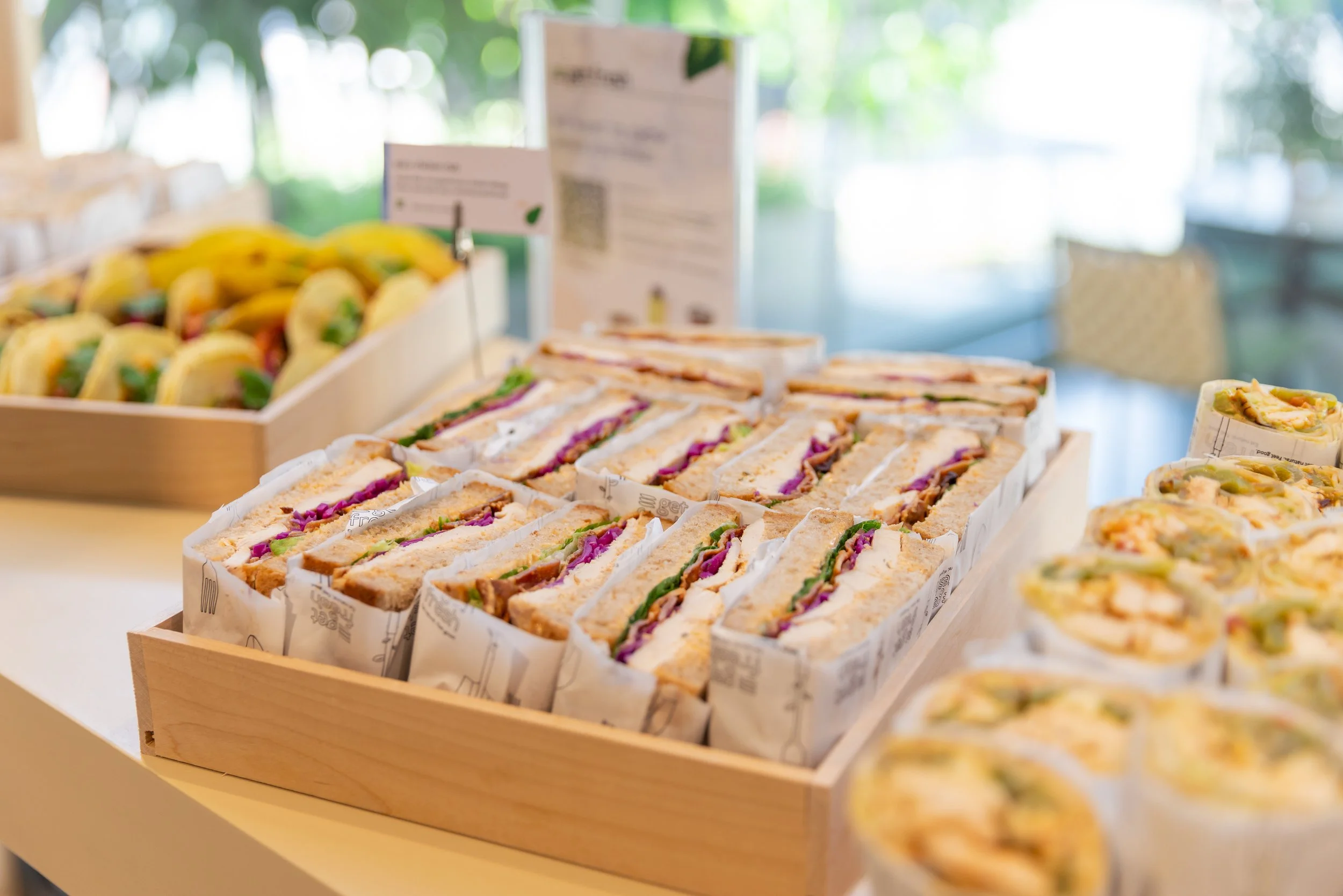 Variety of sandwiches and wraps displayed in a wooden tray, with some visible in the foreground and background.
Healthy sandwich Platters