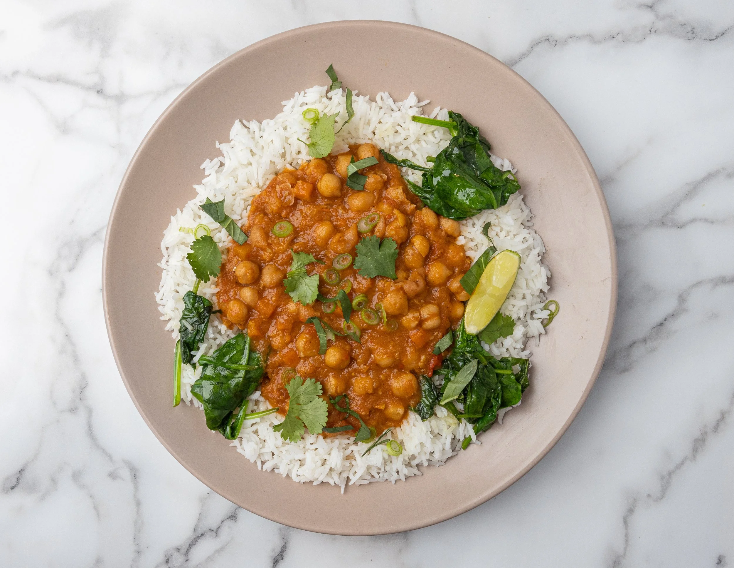 A dish of white rice, chickpea curry, and fresh greens, garnished with cilantro, sliced green onions, and a lime wedge. Healthy, light, nutritious lunch. 