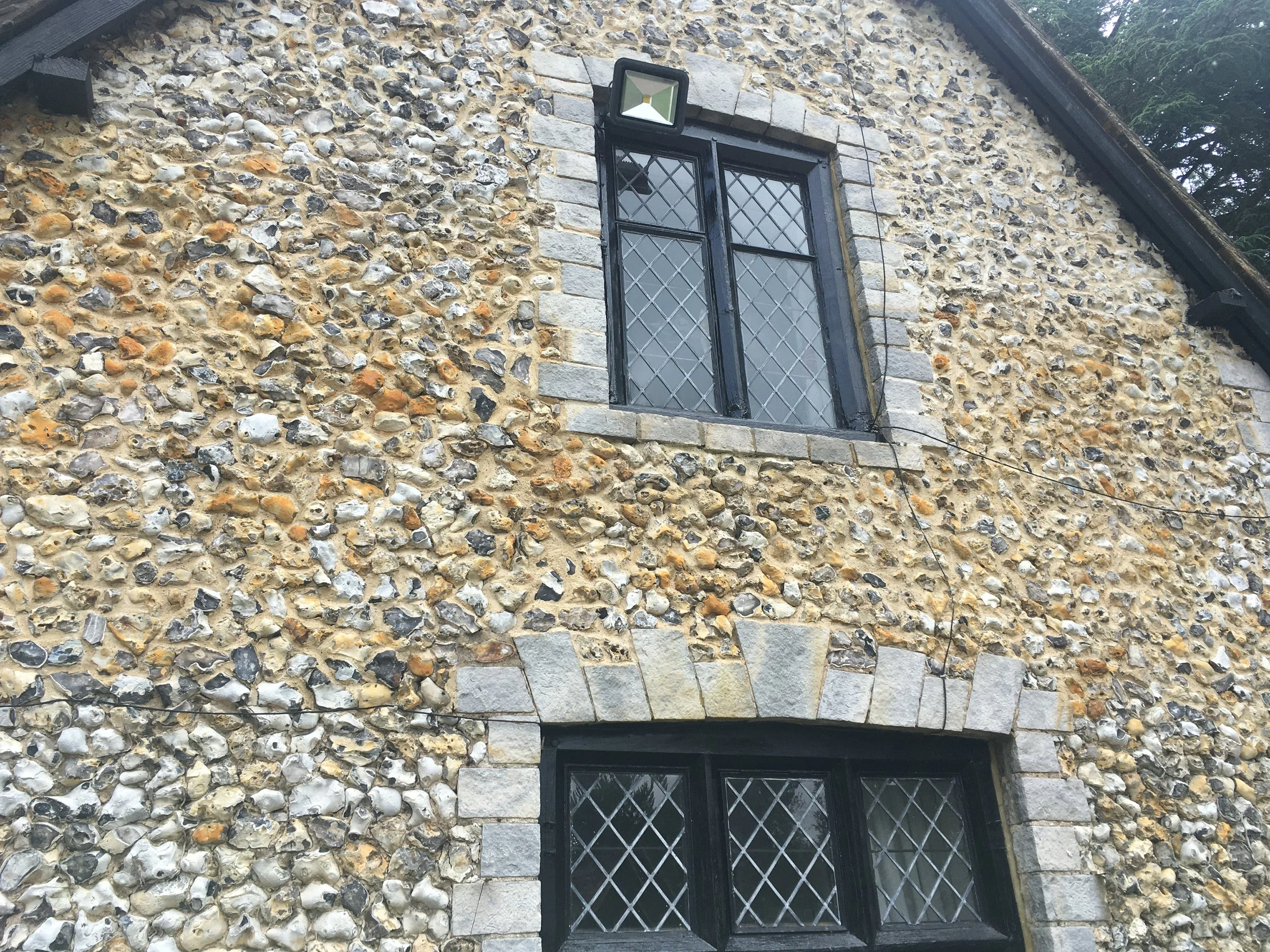 Close-up view of finished Lime and stone cottage wall with a black window frame and diamond-pane glass, topped by a black exterior light fixture.