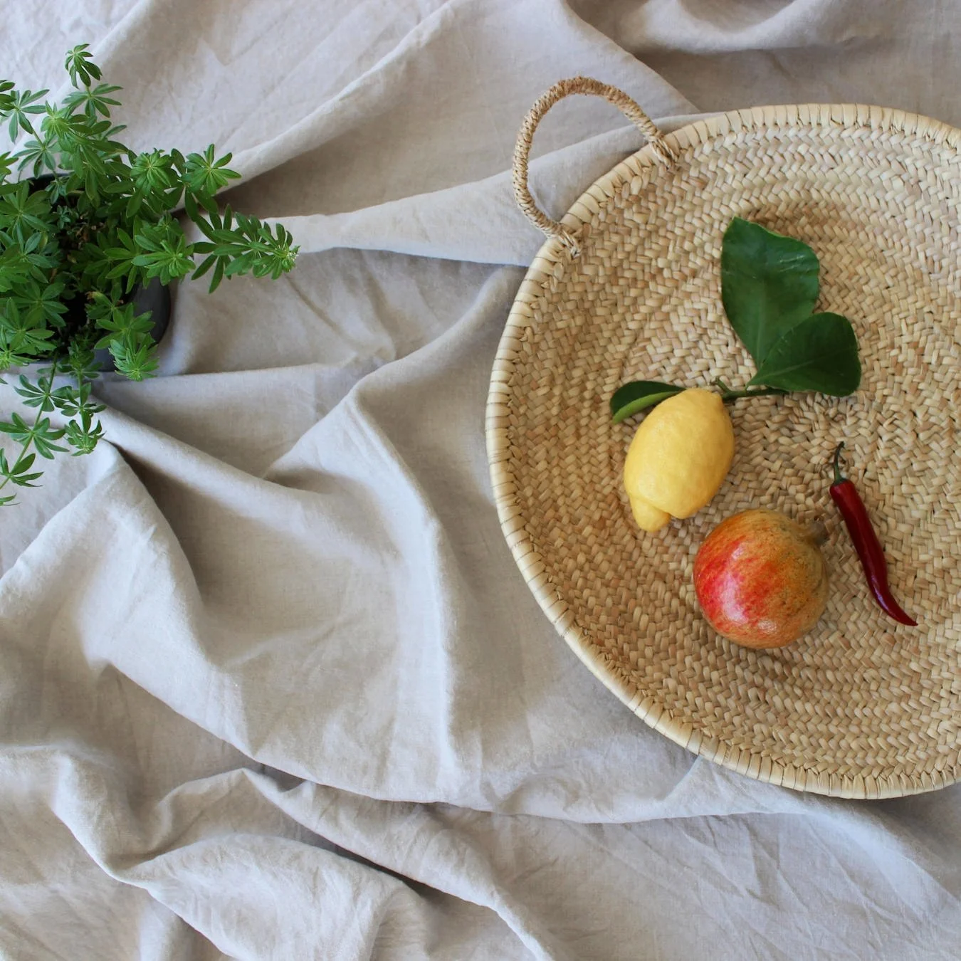 Granatapfel, Zitrone und Chili in einem Korb auf Leinentuch