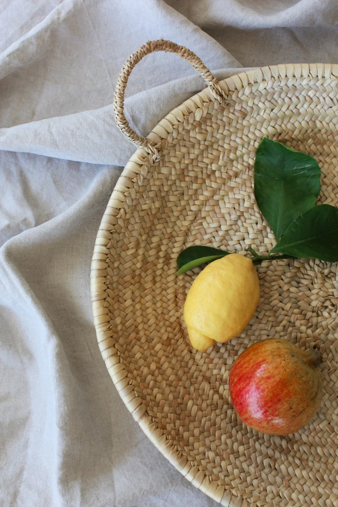 Amalfi-Zitrone und Granatapfel im Flechtkorb auf Leinentuch