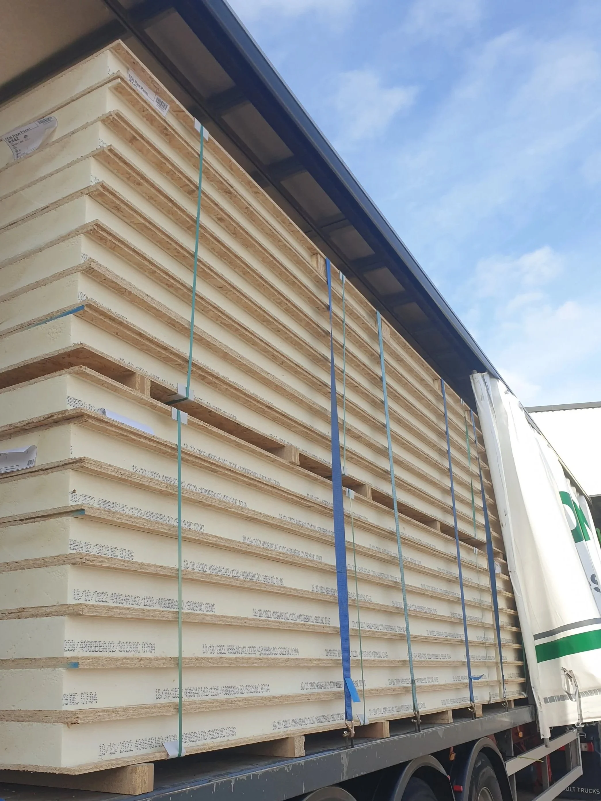 A flatbed truck transporting large sheets of insulation material with a blue sky in the background.