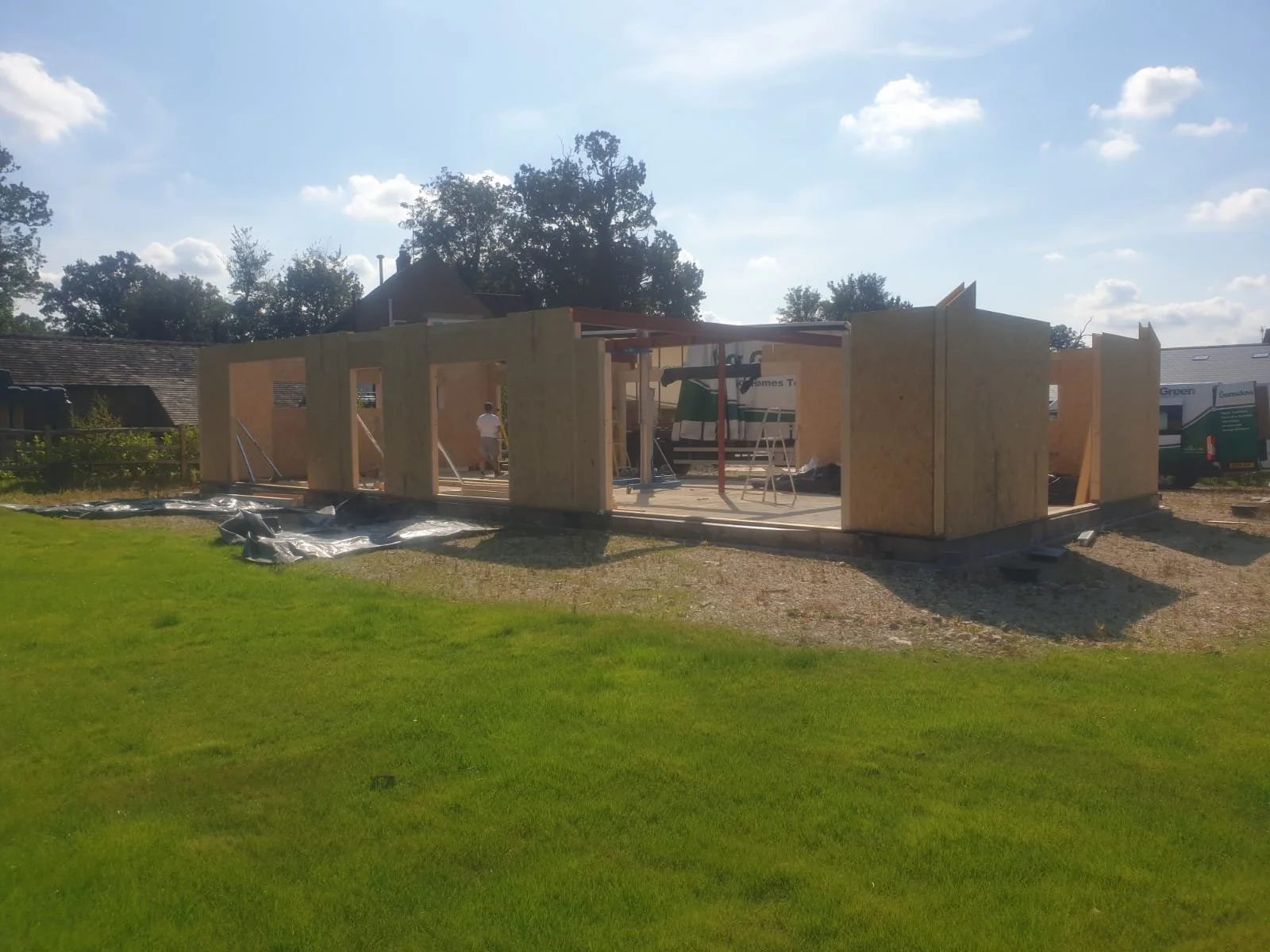 Construction site with wooden framework for a new building under clear sky with some clouds, surrounded by grassy land.