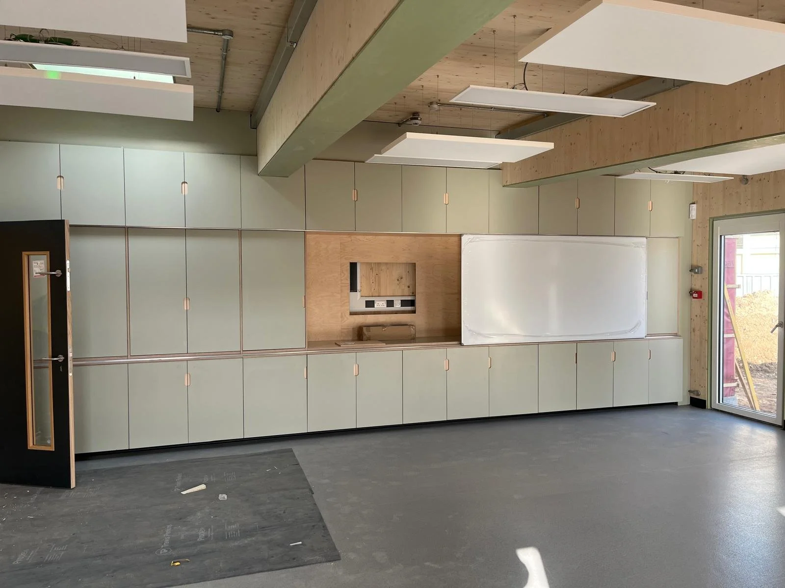 Interior view of a modern kitchen with light green cabinets, wooden accents, whiteboard, and large glass door leading outside.