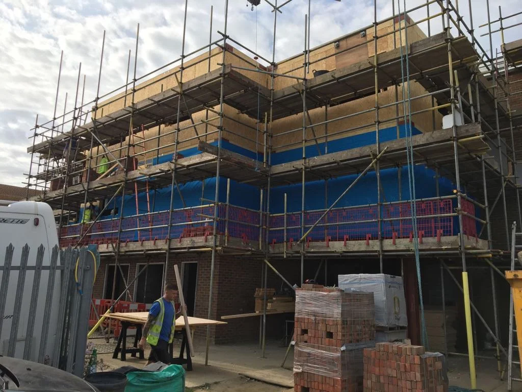 Construction site of a multi-story building with scaffolding, construction materials, and workers present.