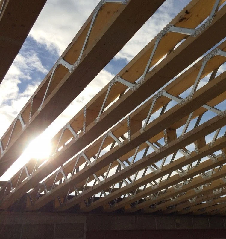 Close-up of wooden construction beams with metal braces, looking up at the sky with sunlight and clouds.