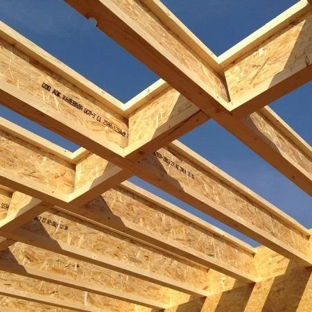 Wooden framing beams of a building under construction against a clear blue sky.