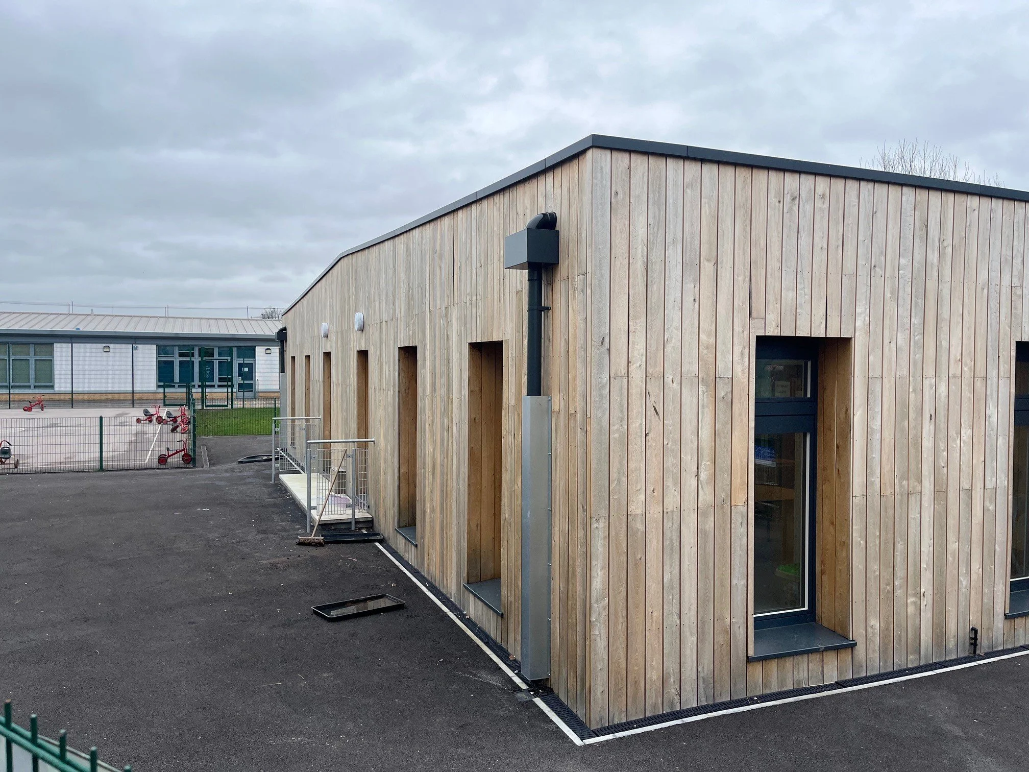 A modern building with wooden exterior siding and multiple windows, with some outdoor bike racks and a paved area.