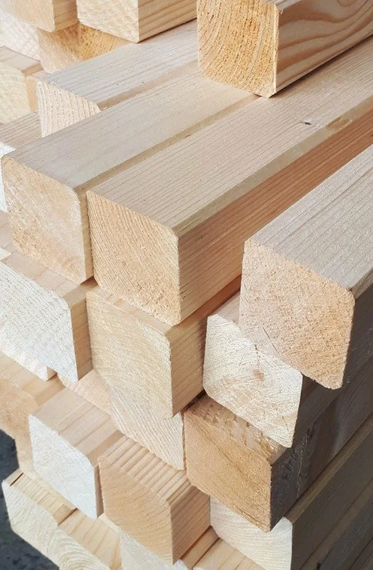 Stacked light-colored wooden planks arranged in a pyramid shape.