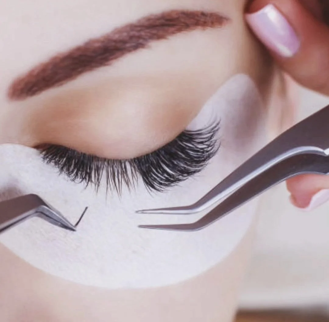 Nahaufnahme eines Auges, das mit Wimpernverlängerung versehen ist. Es gibt einen Künstliche Wimpern-Extension-Werkzeug, das auf die Wimpern aufgesetzt wird.