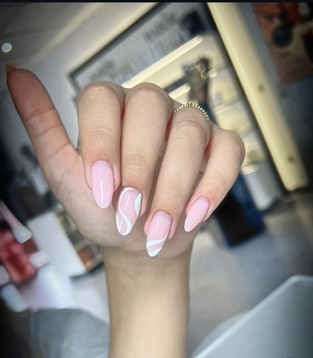 Nahaufnahme von gepflegten, hellrosa und weißen Nageldesigns mit geschwungenen Linien auf den Fingernägeln.