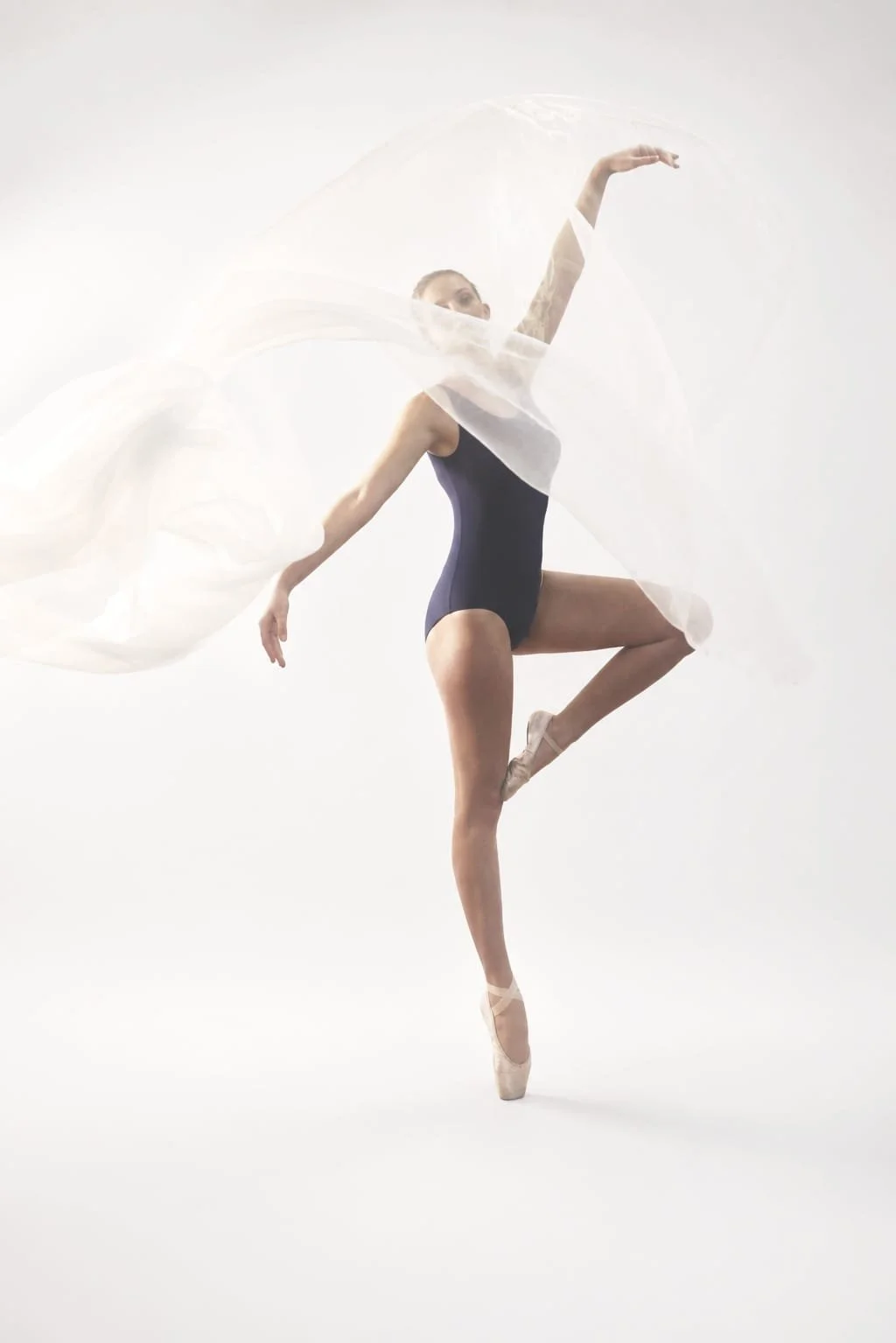Photography by Riaan Swiegelaar. Ballet dancer in navy leotard on pointe with white flowing fabric in a dance pose.