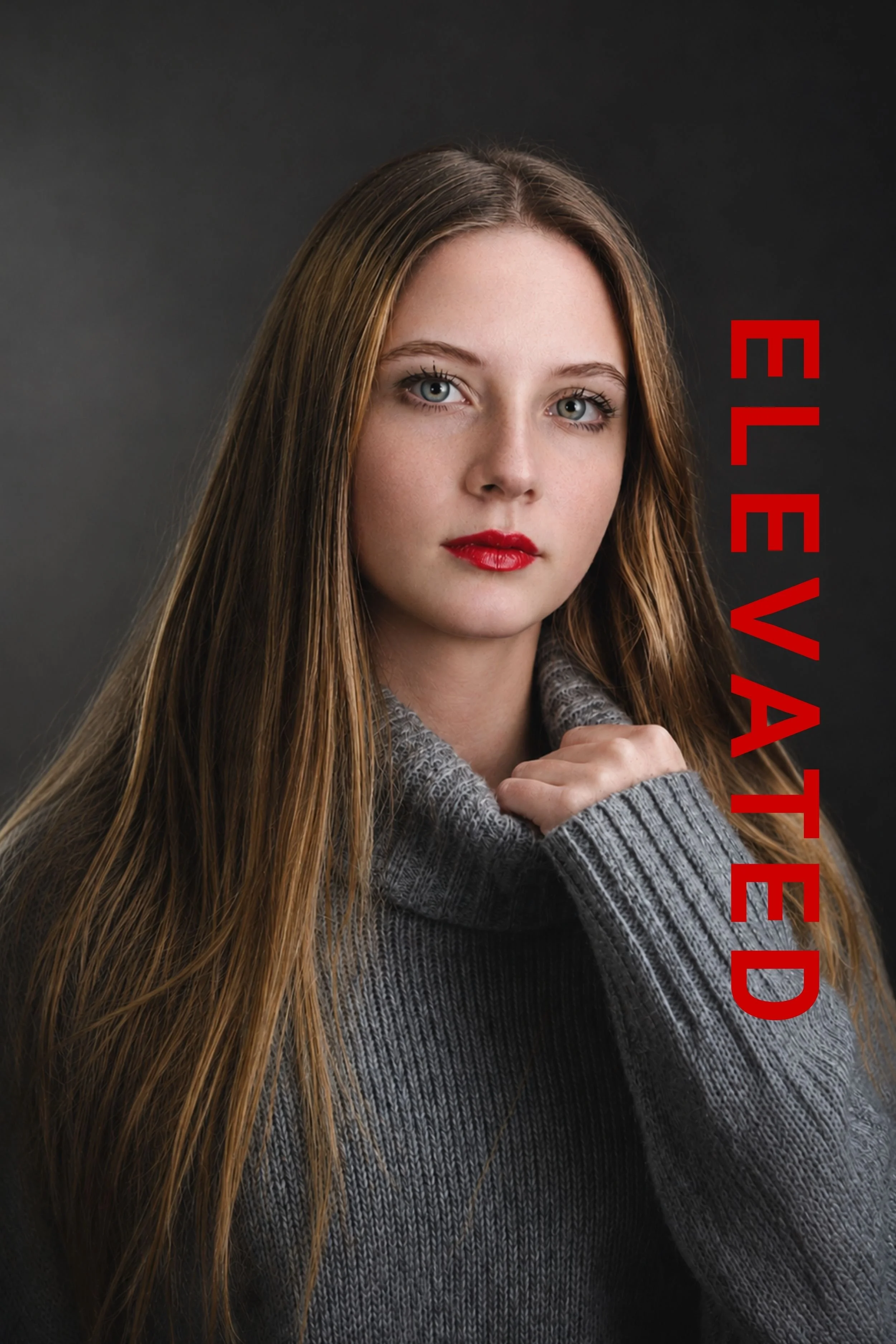 Photography by Riaan Swiegelaar. A young woman with long brown hair, blue eyes, and red lipstick wearing a gray sweater against a dark background. The text 'EL EVI TED' is written vertically in red on the right side of the image.