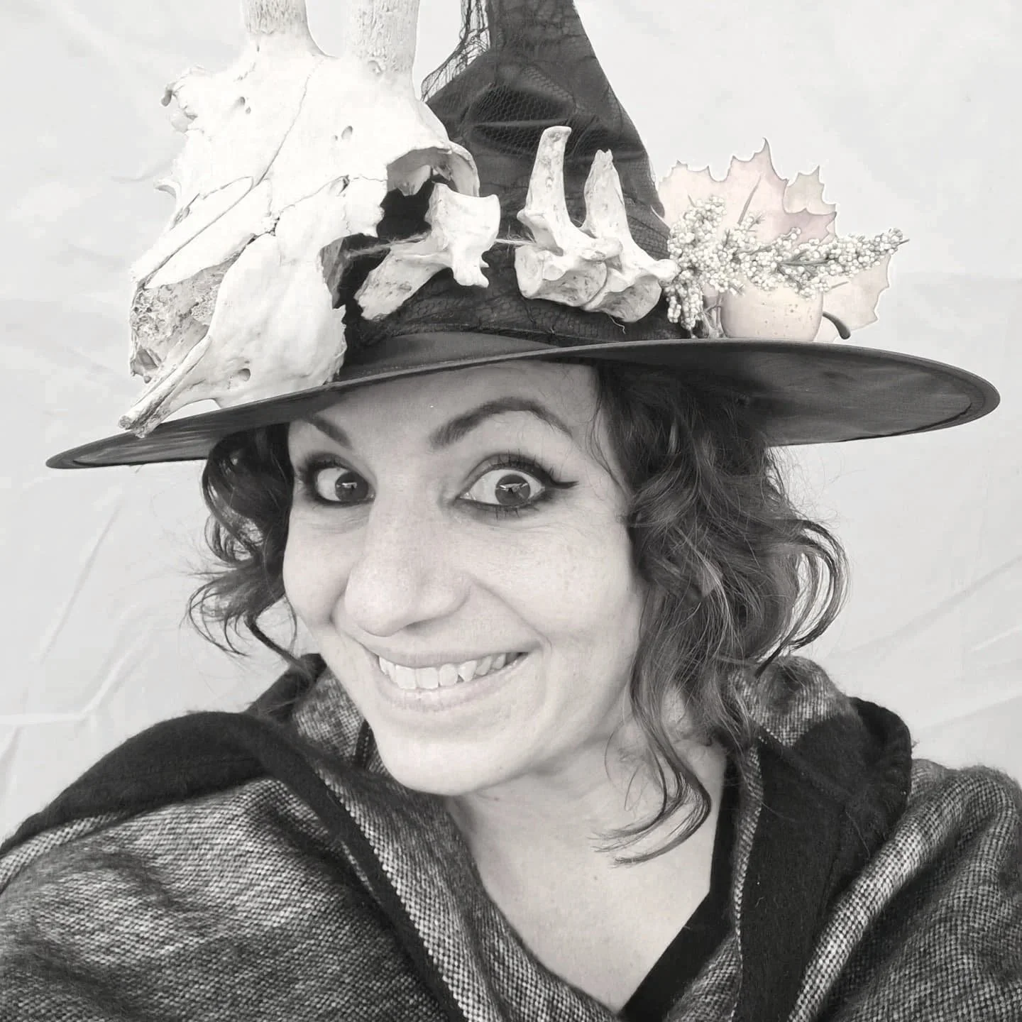 Une femme souriante  (Jessika Geoffroy) portant un chapeau décoré de os, de feuilles et de petites fleurs.