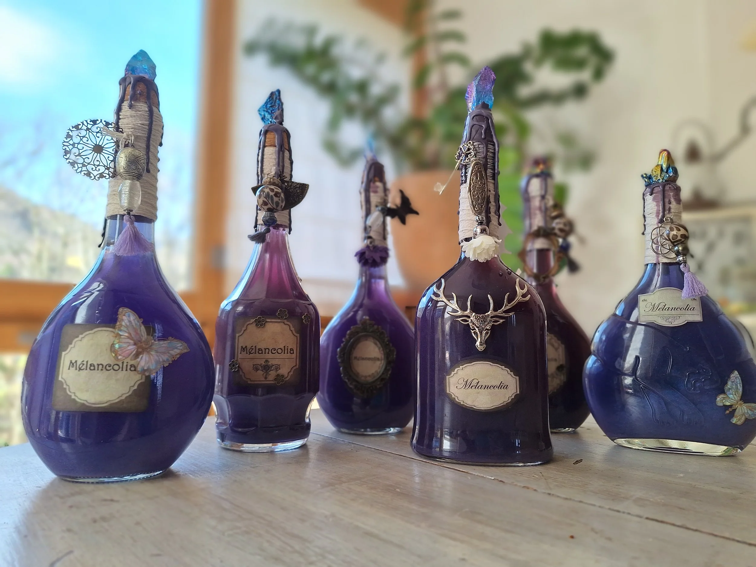 Collection de six bouteilles en verre violettes avec des étiquettes décoratives, ornées de bijoux et d'ornements.