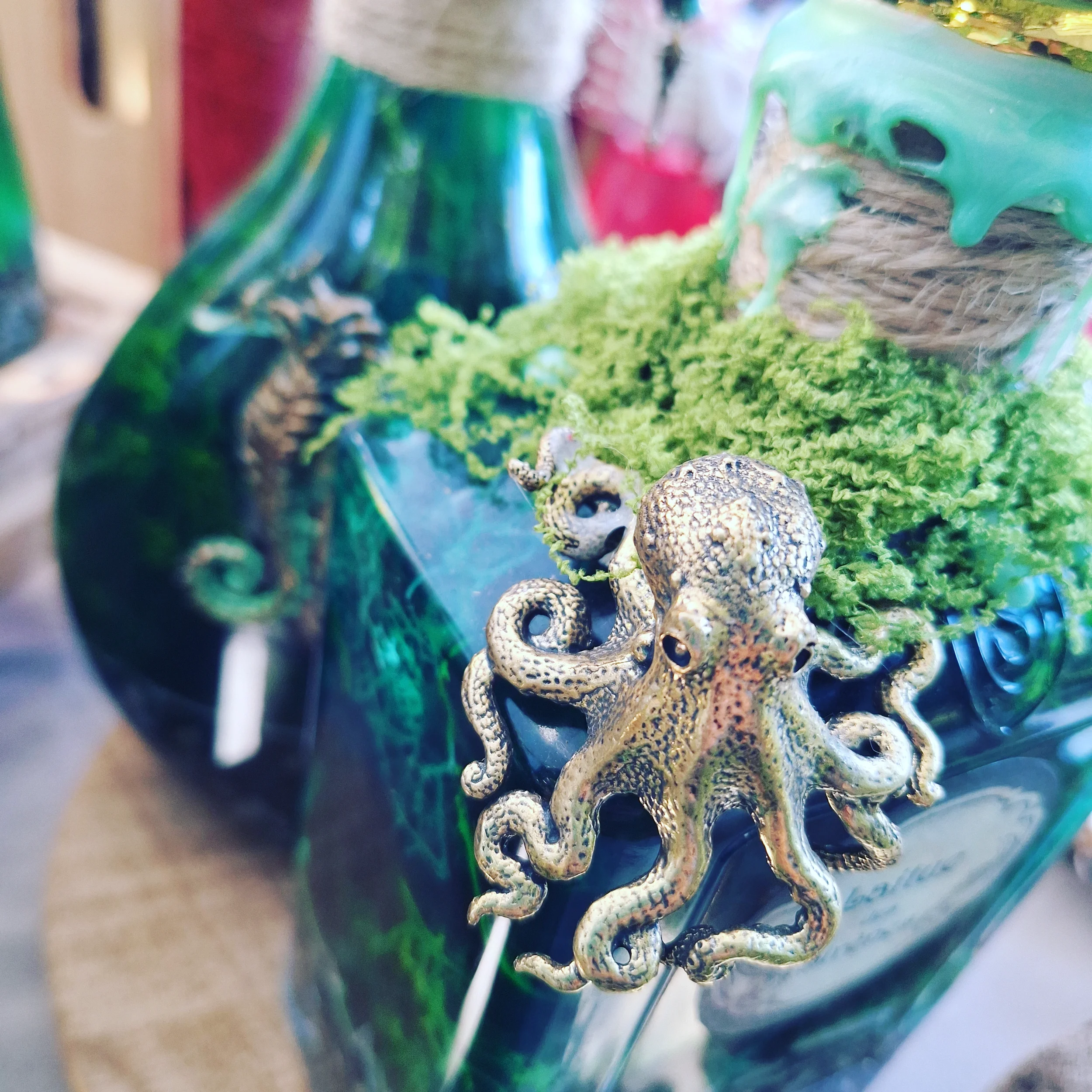 Une décoration contenant une figure de pieuvre en métal, des branches vertes et un vase en verre vert