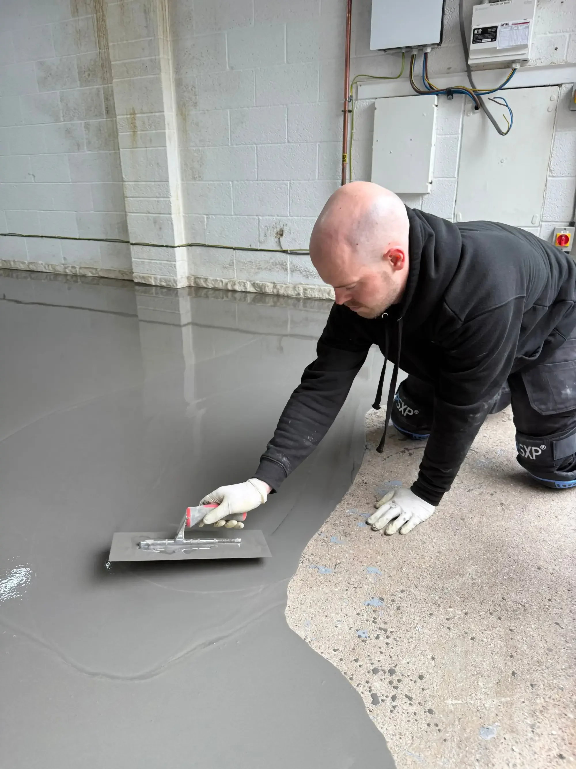A man kneeling on the floor while spreading resin to the floor.