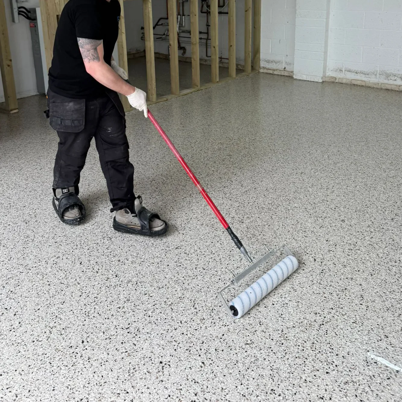 Person applying a coat of resin flooring using a roller tool.