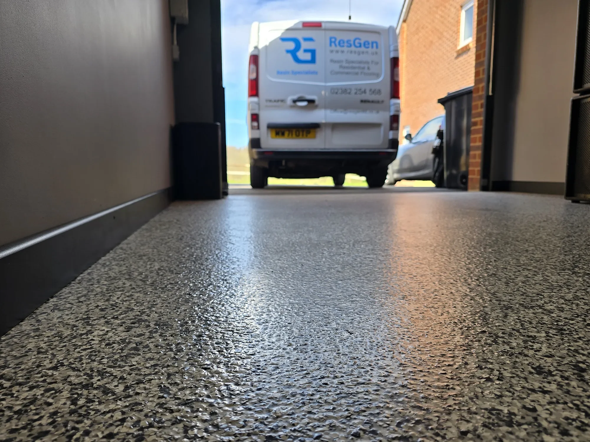 View from a low angle of a newly finished garage resin flooring, looking out through an open door at a ResGen's van parked outside.