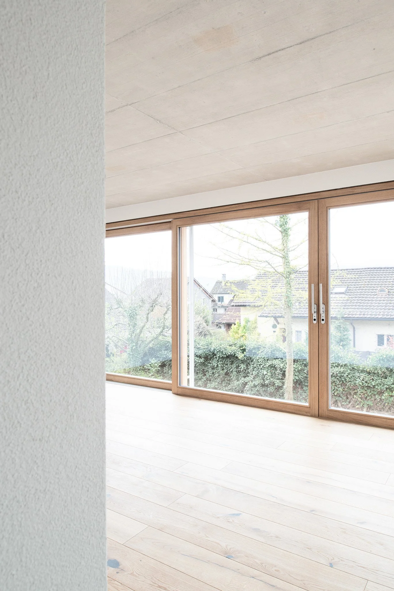 Innenansicht eines Raumes mit grossen Holztüren und Blick nach draussen auf ein Wohngebiet mit Bäumen und Dächern.