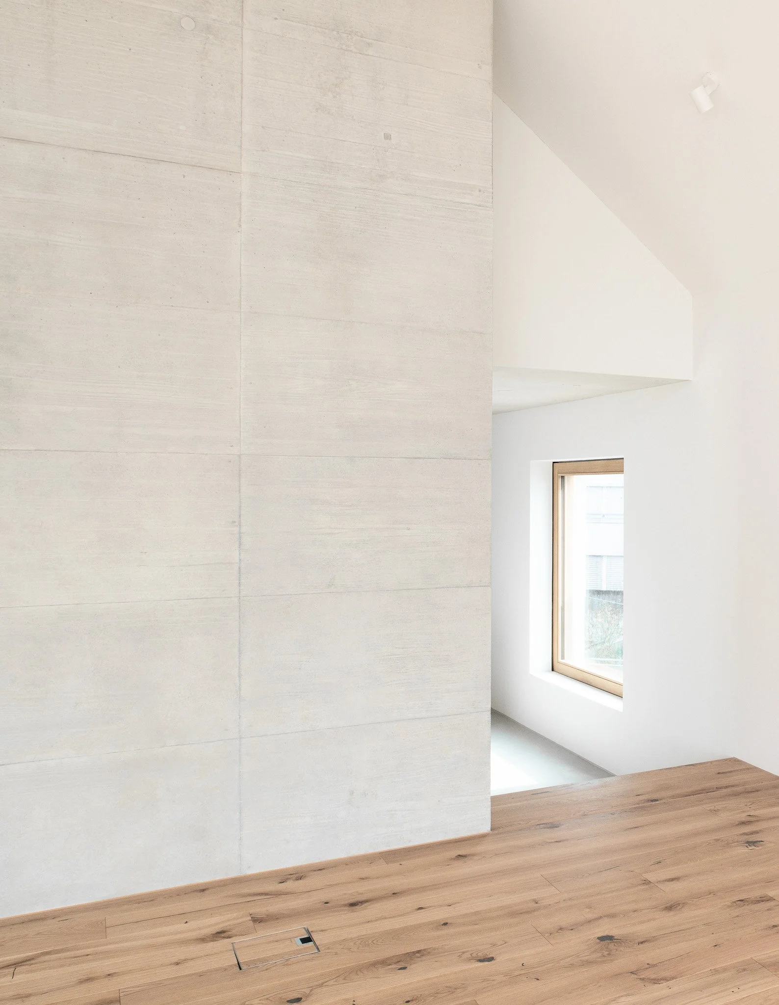 Ein hell erleuchteter Raum mit weissen Wänden, Holzfussboden und einem Fenster, das Tageslicht hereinlässt.