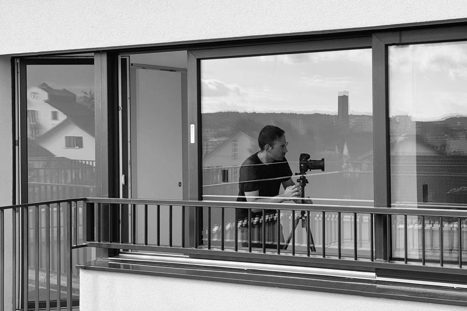 Nicolò Di Giovanni Architekturfotograf fotografiert durch ein Fernglas auf einem Balkon, im Hintergrund Stadt und Berge, Schwarz-Weiss-Foto.