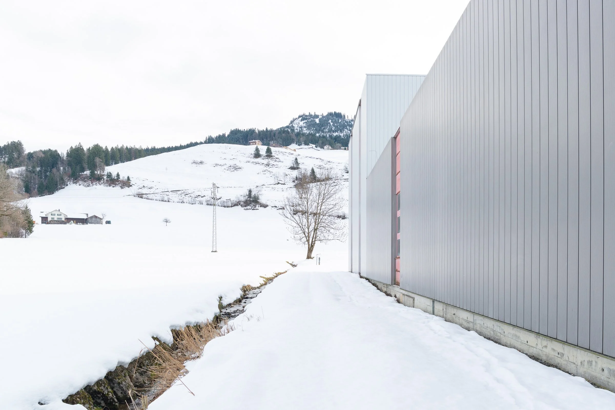Moderne Gebäude mit silberner Fassadenwand neben einer verschneiten Landschaft und Berg im Hintergrund.