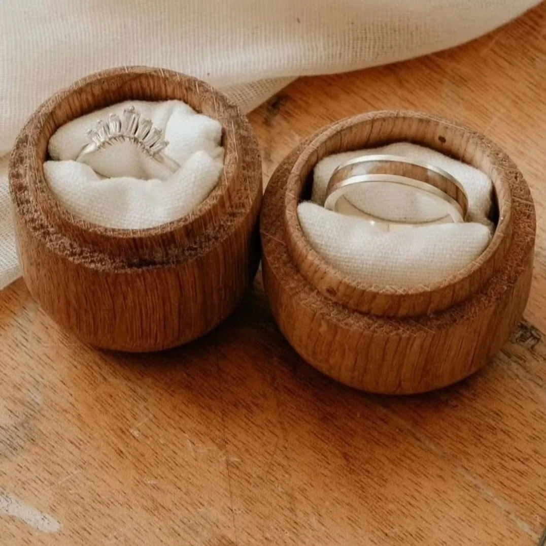 Two wooden ring boxes with rings inside, one with a silver band and the other with multiple stacked rings, placed on a wooden surface.