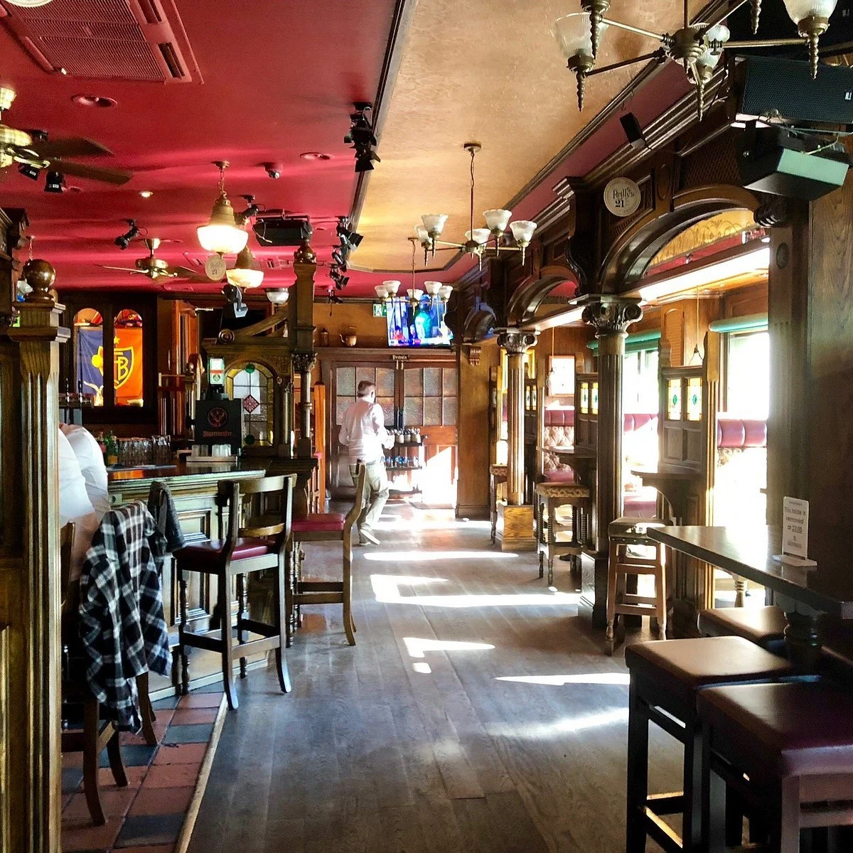 Innenaufnahme eines traditionellen Pubs mit Holzvertäfelung, gemütlichen Sitzecken, Barbereich, Hängelampen, Tageslicht durch Fenster, einige Mitglieder der Crew und Fernseher an der Wand.