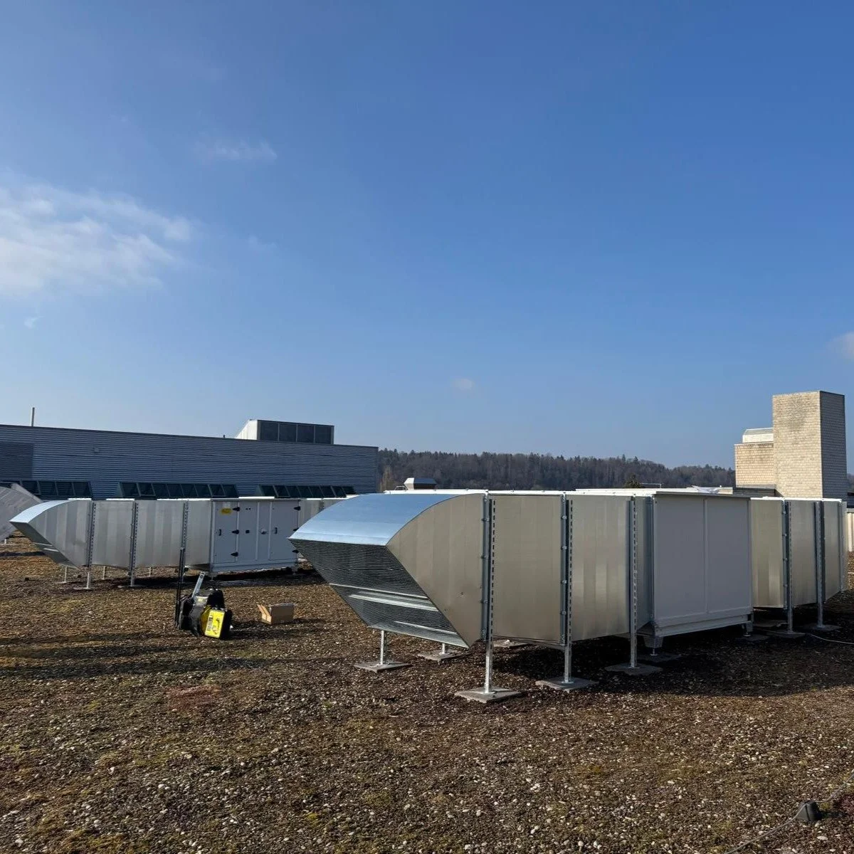 Blick auf die Dachlüftungs- und Klimaanlagen auf einem Dach eines Gebäudes, mit blauem Himmel im Hintergrund.