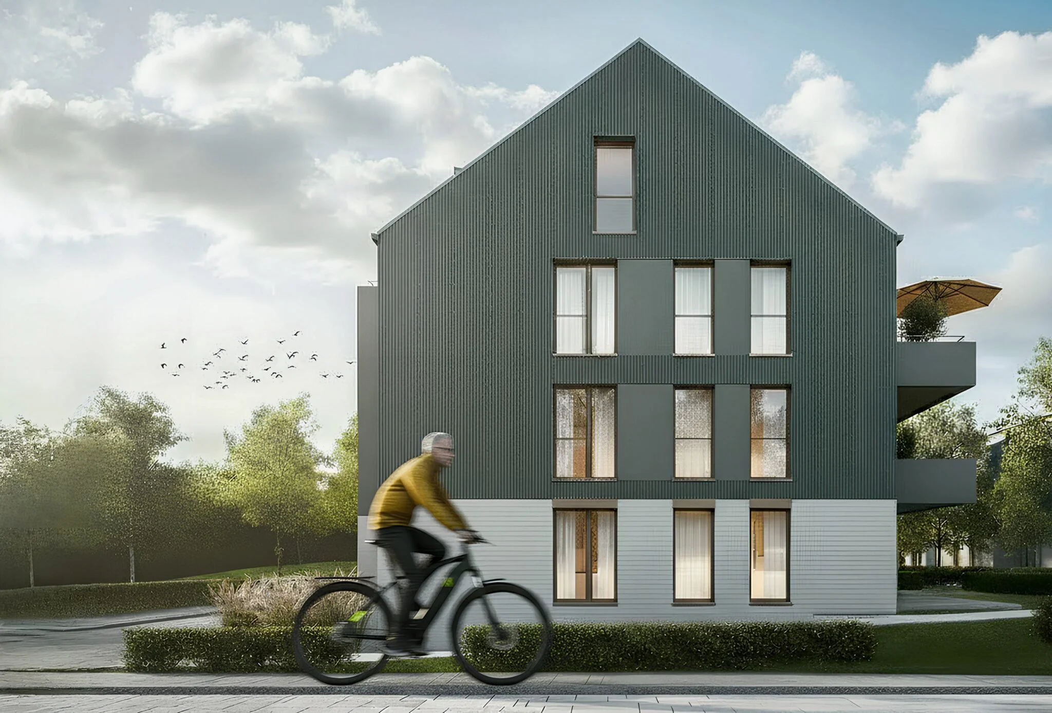 Mehrstöckiges, modernes Haus mit dunklem Außenwandverkleidung, großen Fenstern und einem Balkon mit Sonnenschirm. Ein radfahrender Mann in gelbem Pullover fährt auf der Straße vorbei, im Hintergrund Himmel mit Wolken und Bäumen.