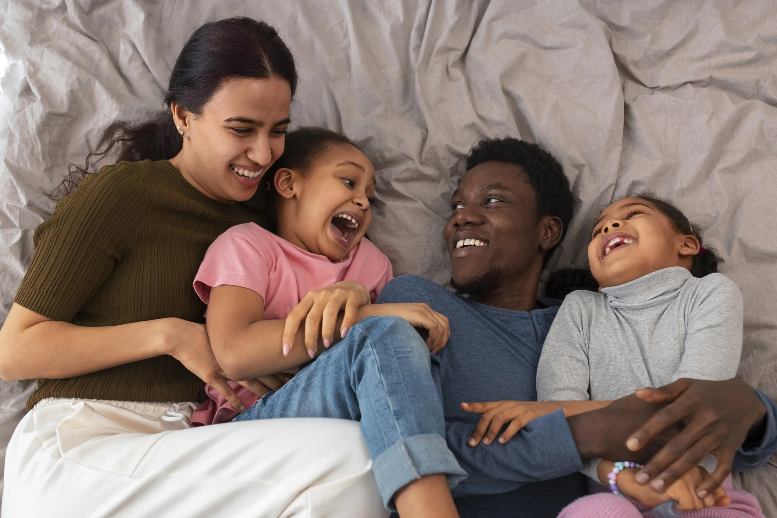 A family of five lying on a bed, smiling and laughing together.