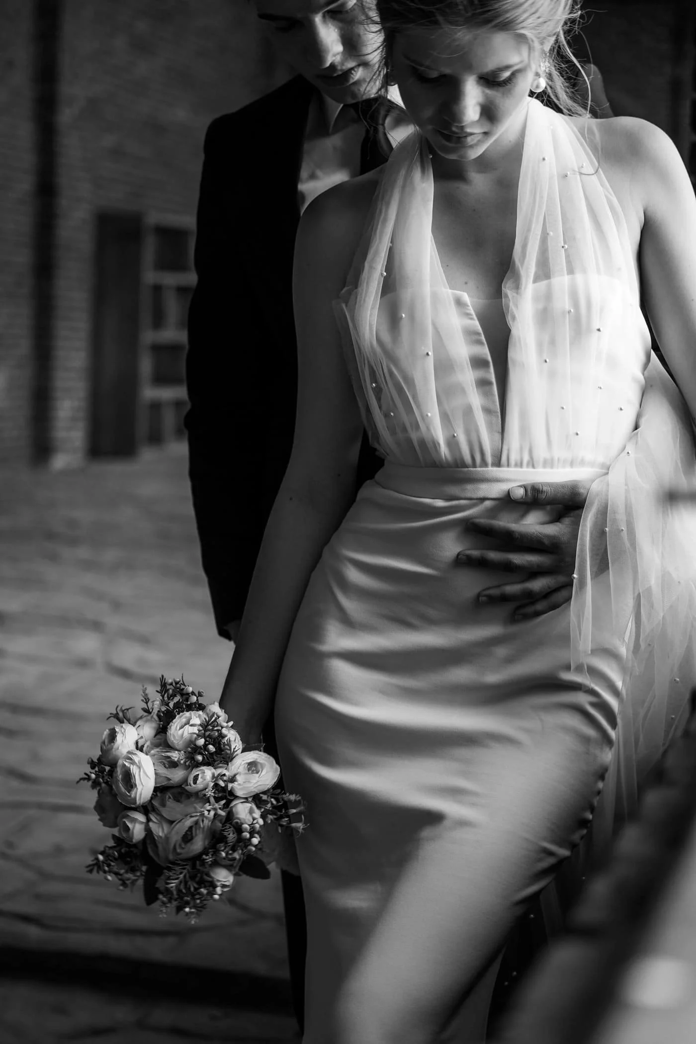 A bride holding a bouquet of flowers, with a person behind her gently touching her waist.