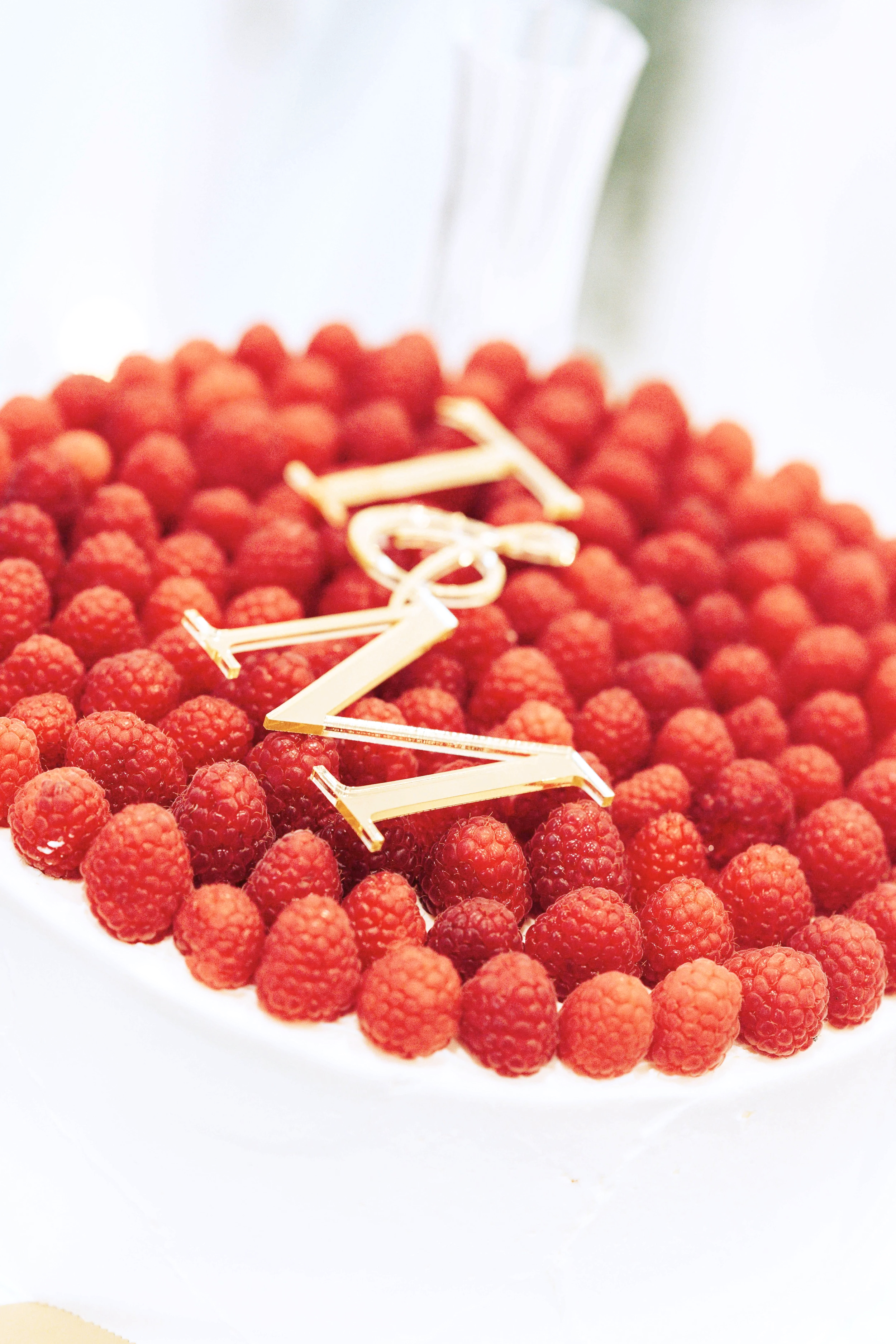 A cake decorated with fresh raspberries and a gold 'Happy Birthday' topper.