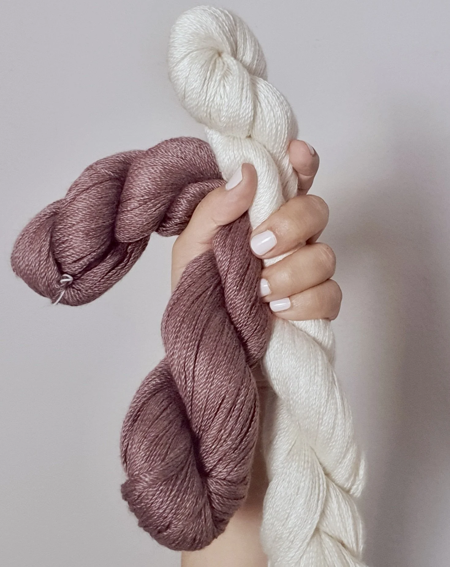Hand hält drei Stränge Handgestricktes in Weiß, Rosa und Braun.