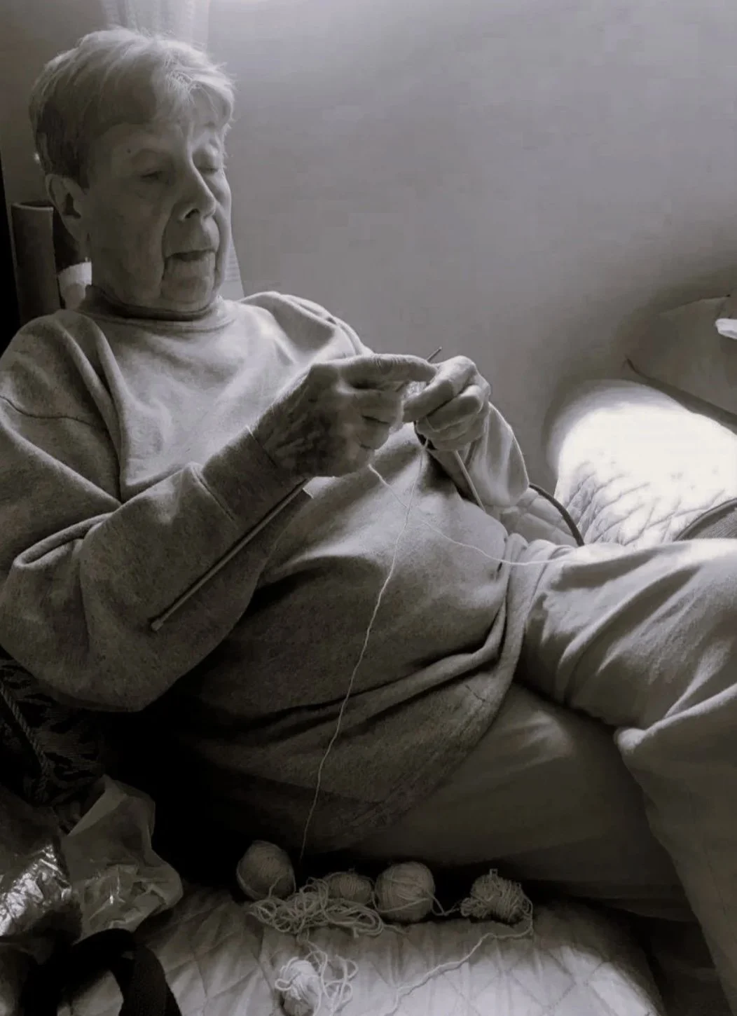 Älterer Mann liegt im Bett und strickt mit Nadeln und Wolle.