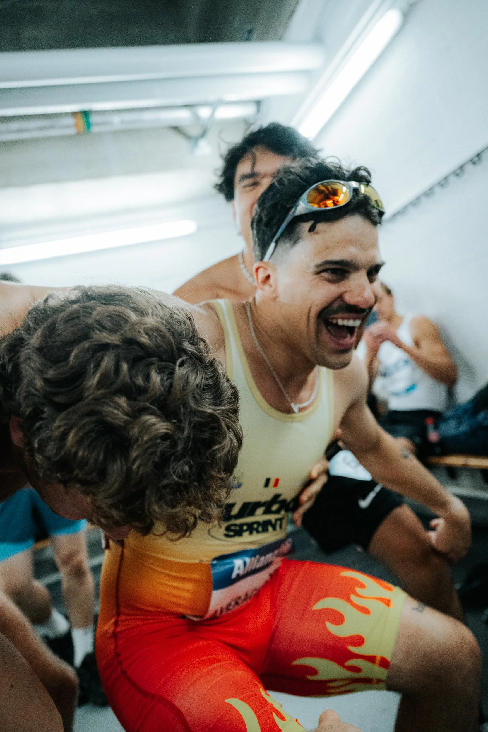 Two male runners in racing gear smiling and celebrating inside a locker room after a race.