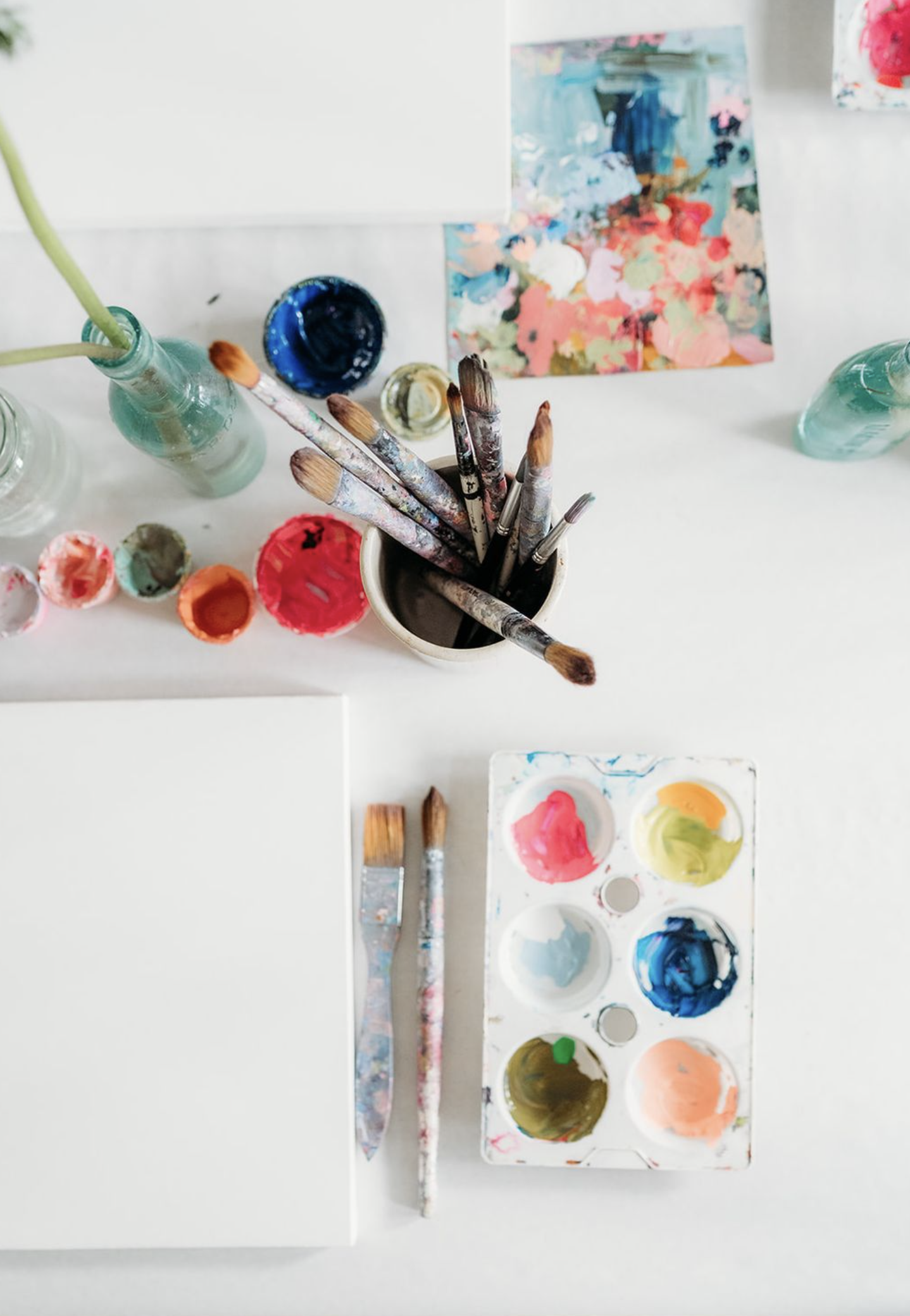 Assorted watercolour paints, paintbrushes, and an abstract painting on paper as part of a creative workshop.