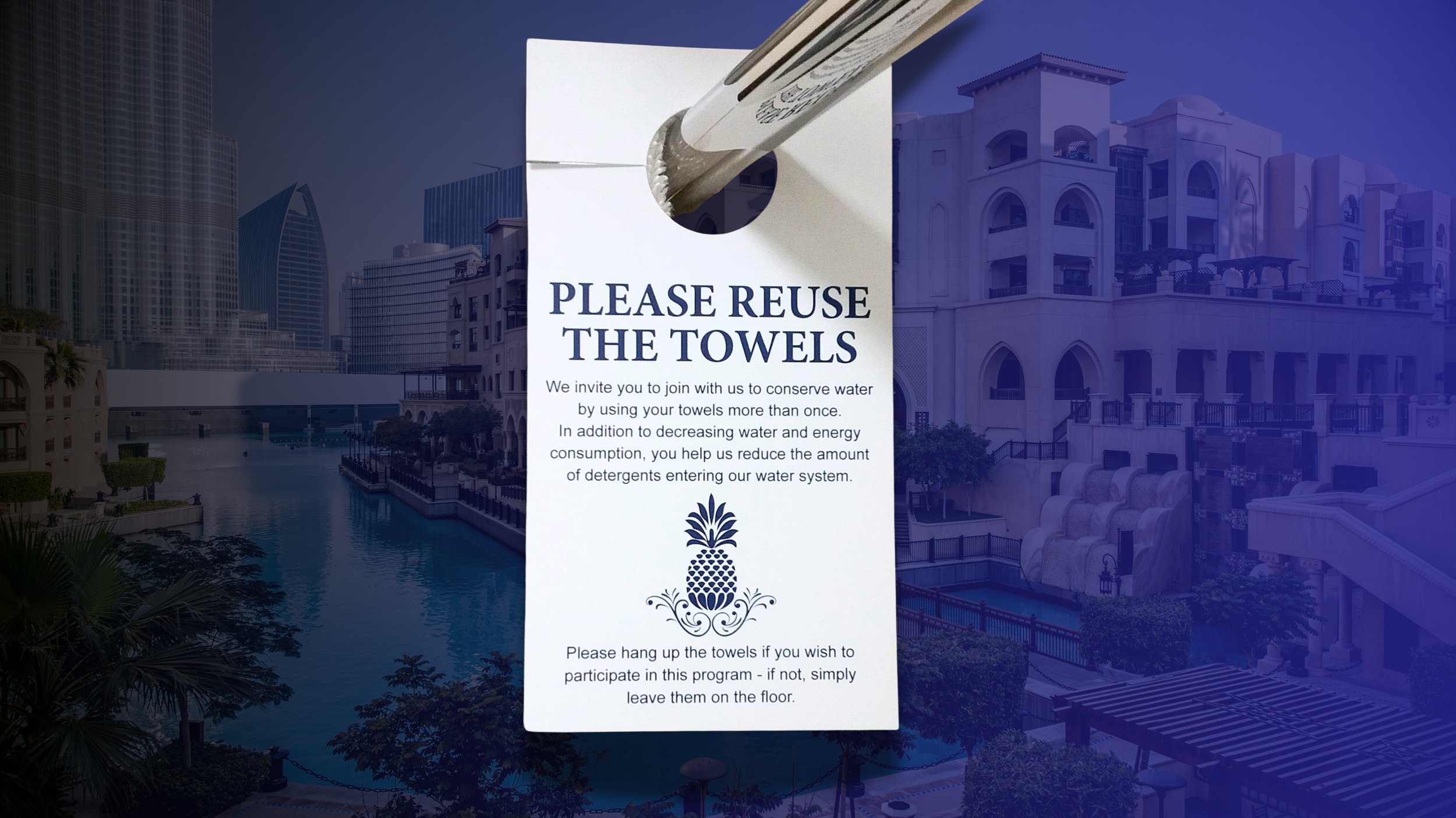 Sign requesting towel reuse in a hotel or resort with a pool and modern buildings in the background.