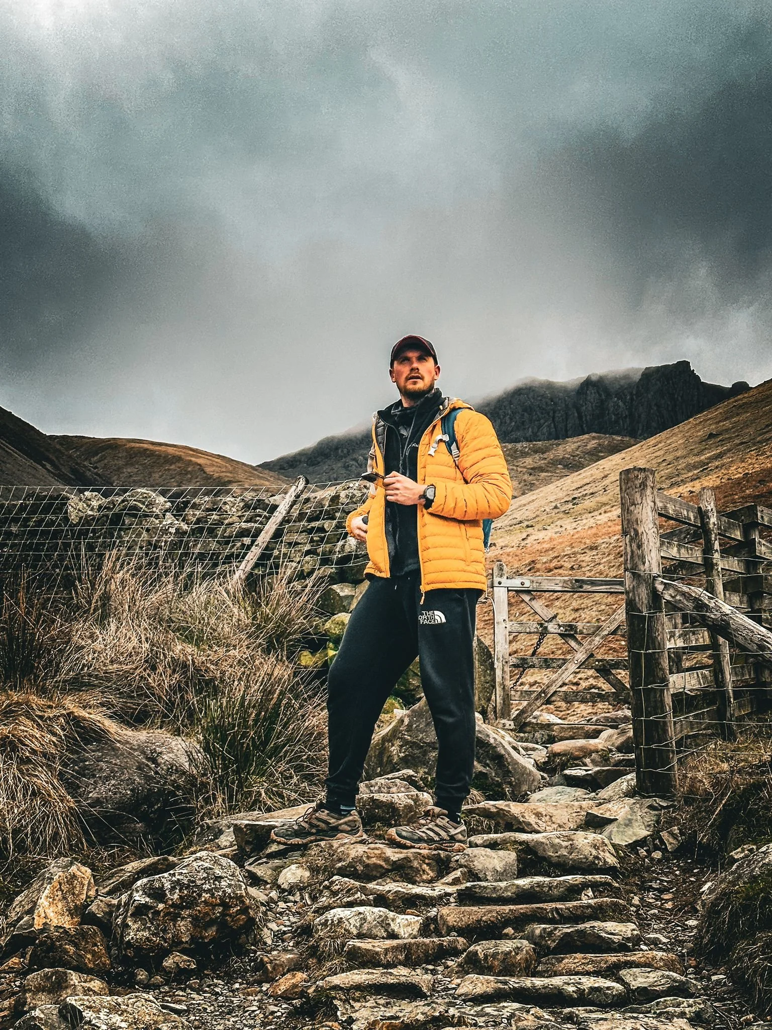 A man hiking on a rocky trail in a mountainous area with dark, overcast skies.