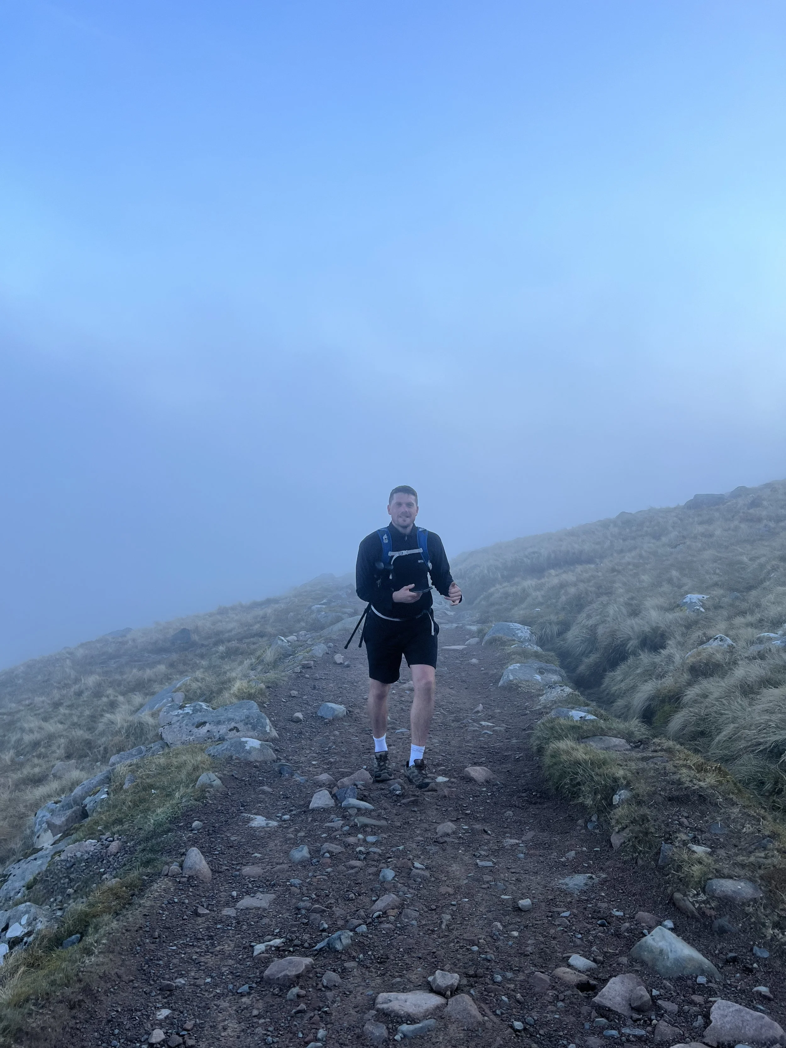 A man hiking on a foggy mountain trail surrounded by grass and rocks.