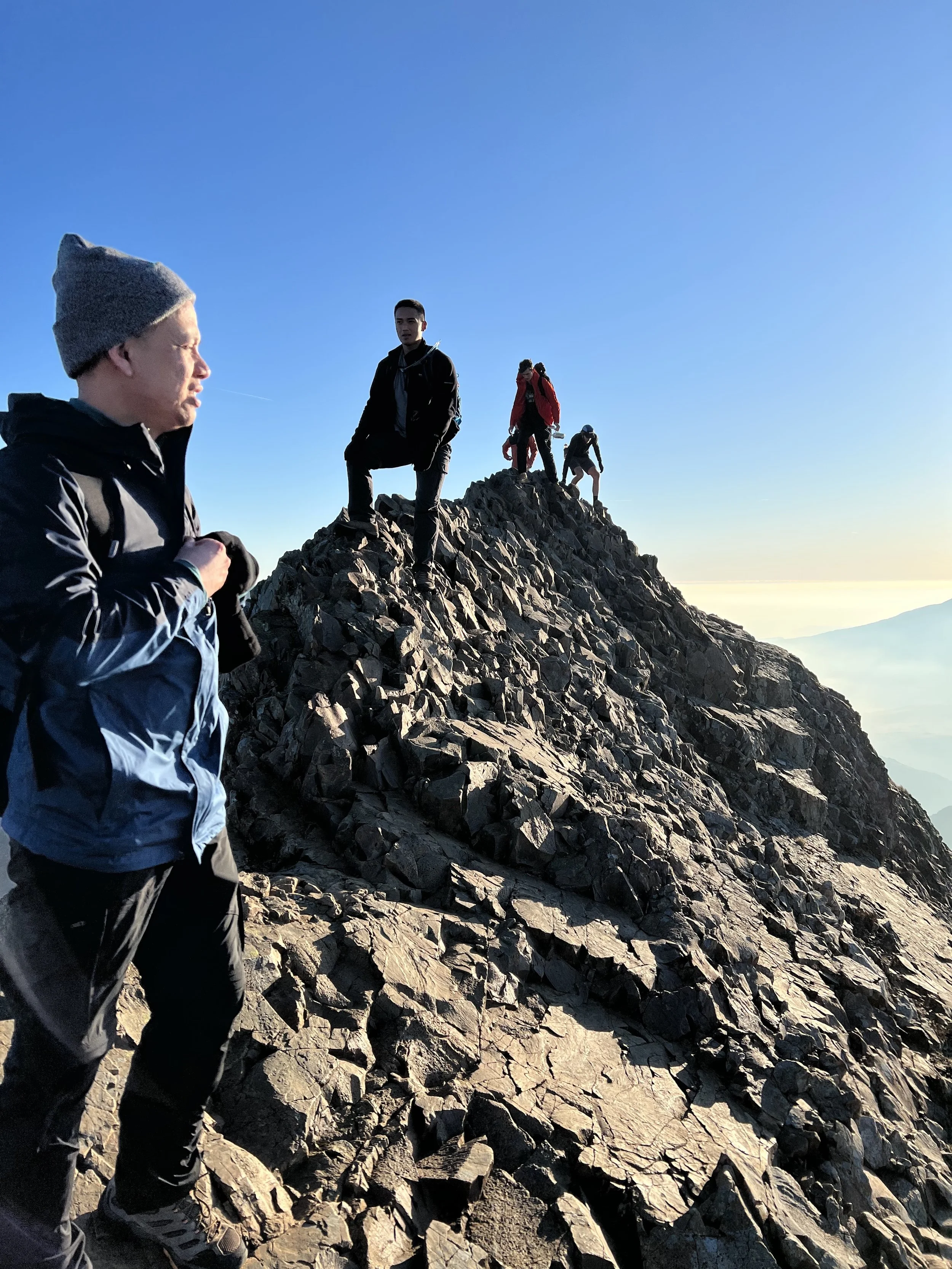 Group of hikers climbing a rocky mountain peak during the day with clear blue sky.