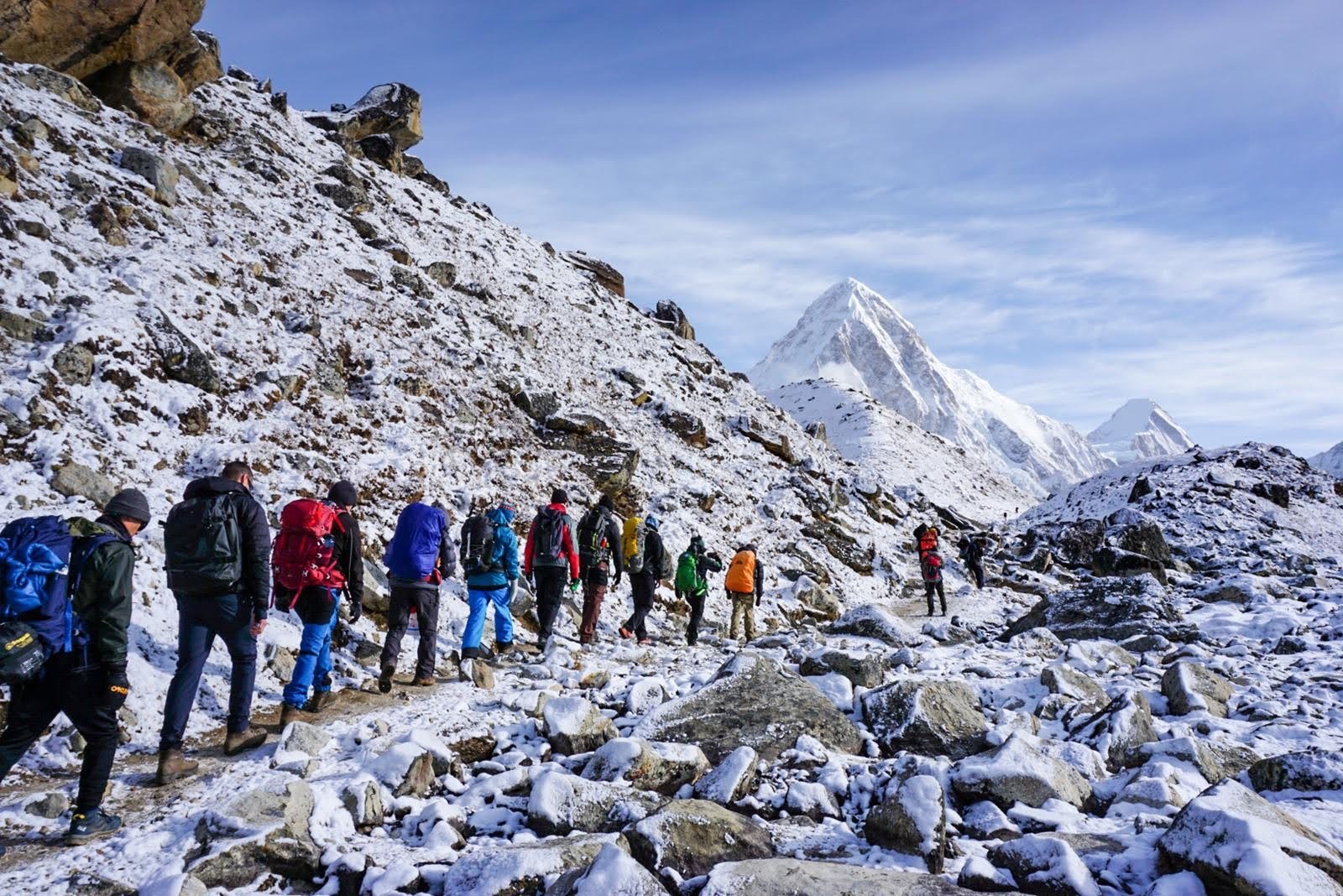 A group of hikers trekking through a snowy mountain landscape with snow-covered peaks in the background.