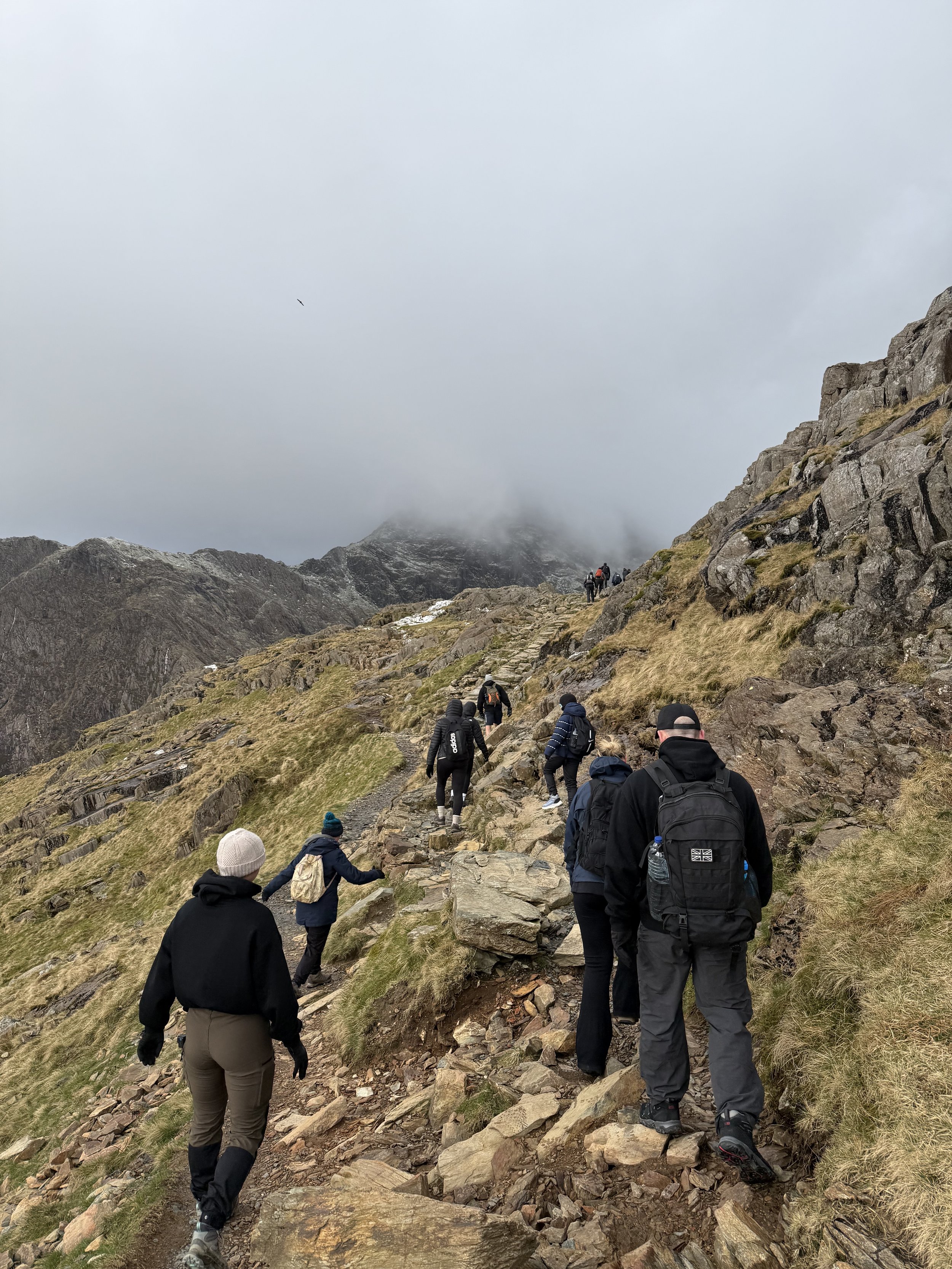 Group of hikers climbing a rocky mountain trail under cloudy sky.