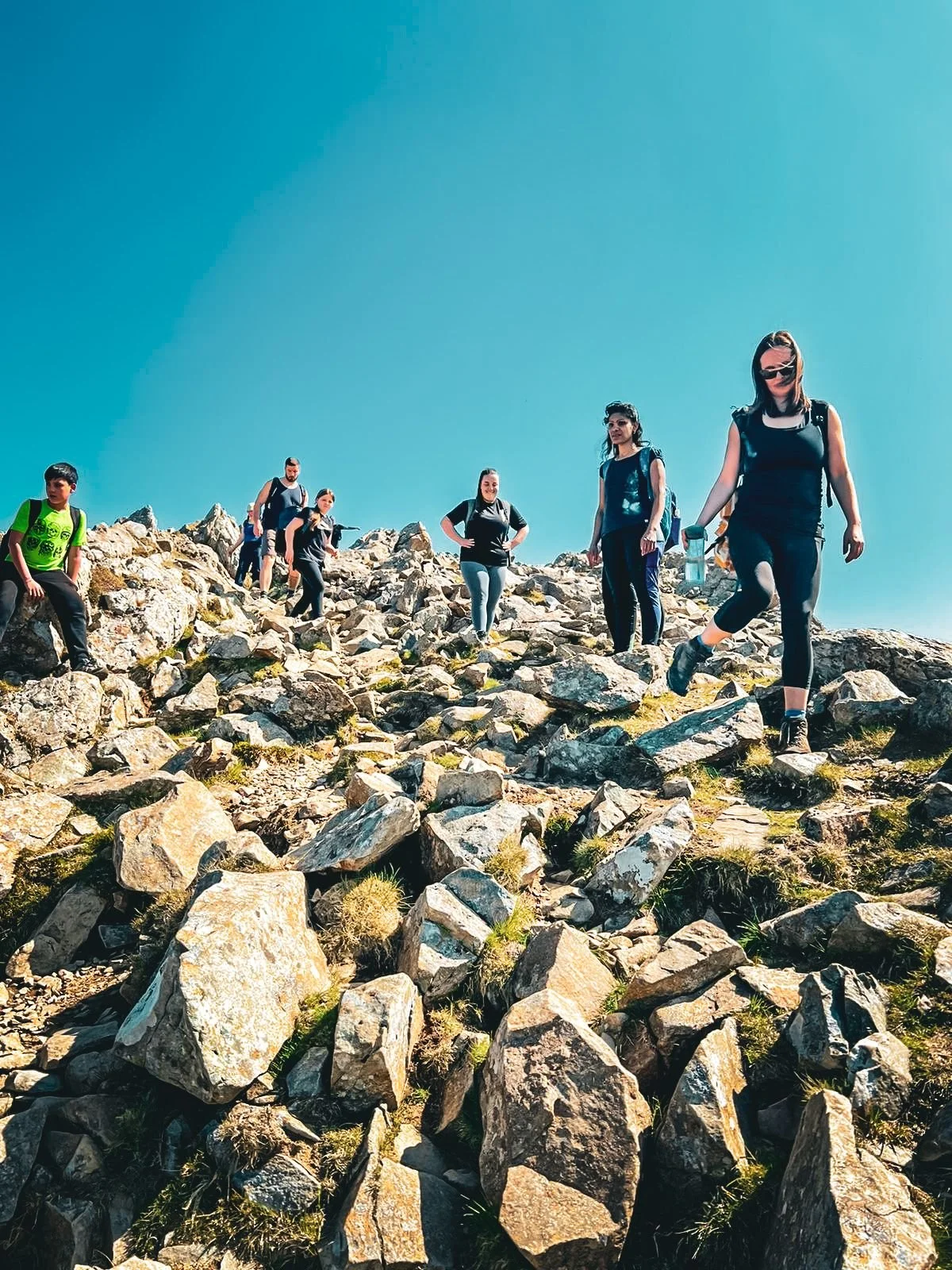Group of people hiking on rocky terrain in a mountainous area under a clear blue sky.