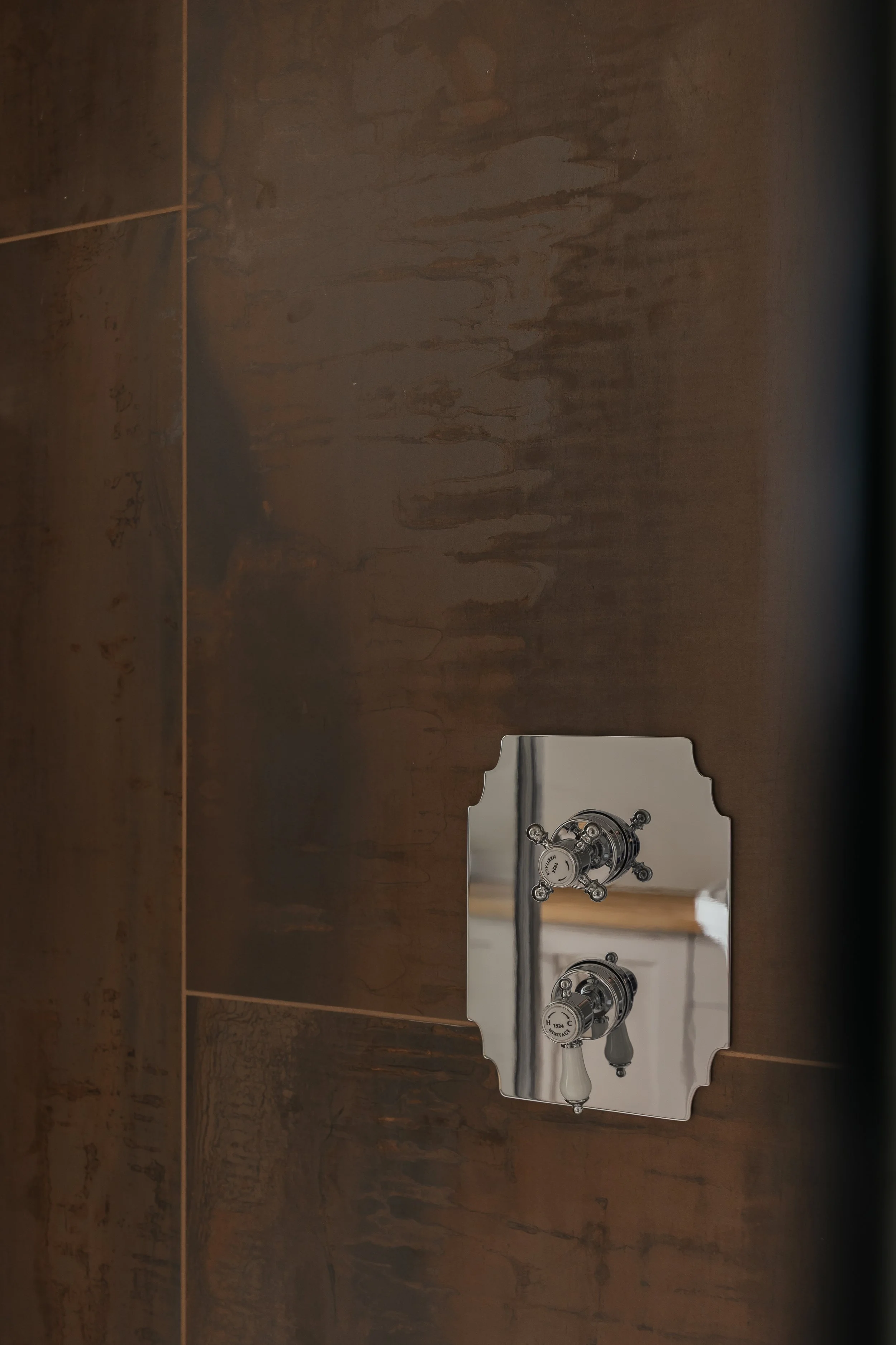 A bathroom mirror with dual faucets reflected in a mirror on a wooden wall.