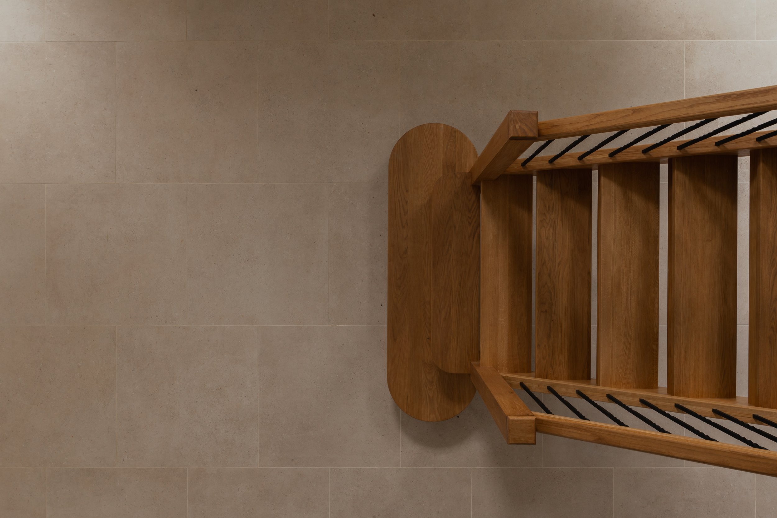 Top view of a wooden bench with a slatted backrest and a round wooden support at the front, against a beige tiled floor.