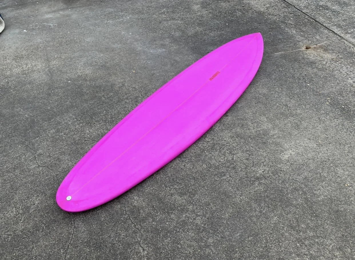 Pink surfboard lying on gray pavement.