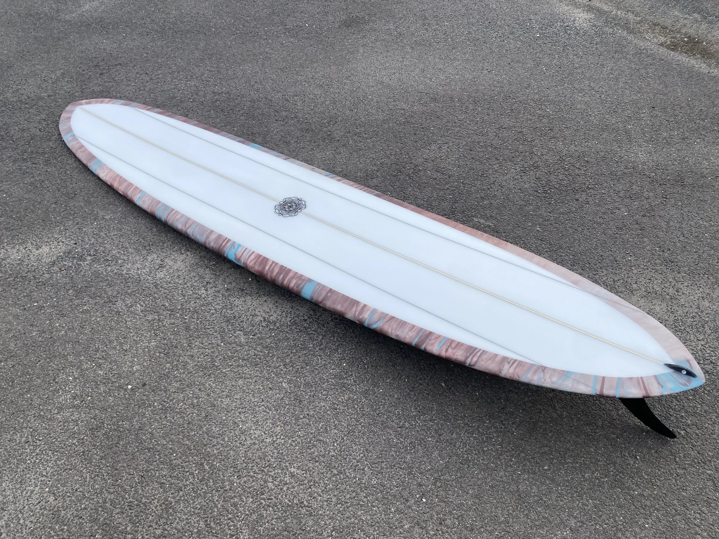 A white surfboard with colorful accents on the edges, lying on a paved surface.