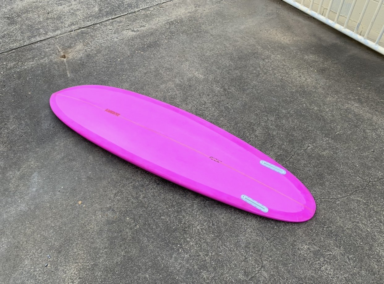 Pink surfboard lying on a concrete ground near a white barrier.